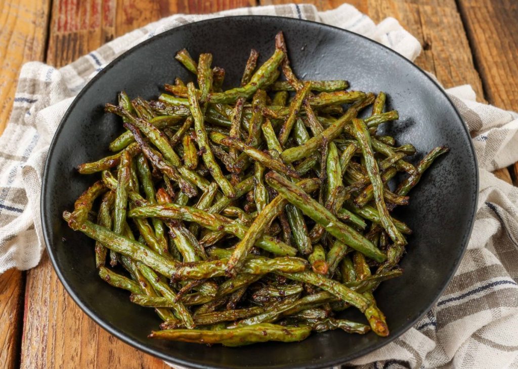 Roasted green beans in black bowl on wooden table