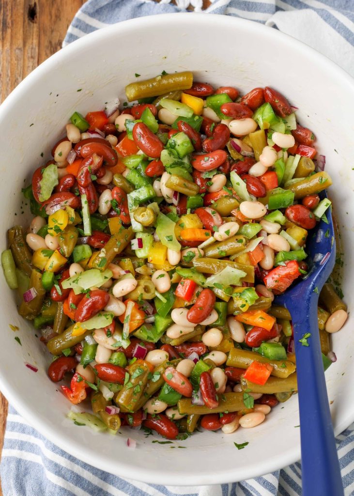 beans, bell peppers, and onions with dressing in white bowl with blue spoon