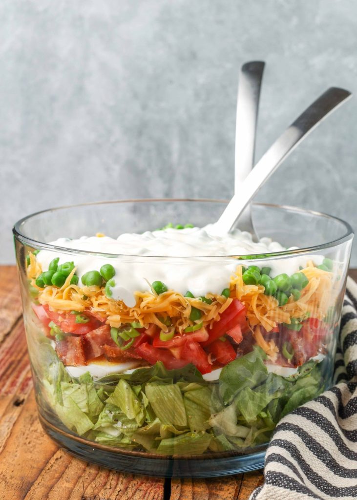 salad in clear bowl with dressing on top with tongs in bowl
