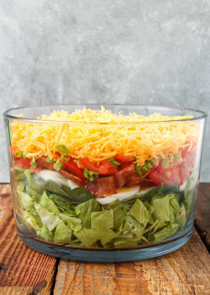 cheese topped salad in clear mixing bowl on wooden table