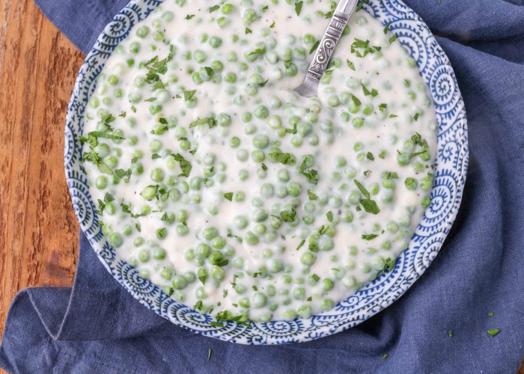 peas with a cream sauce in a blue and white bowl with spoon
