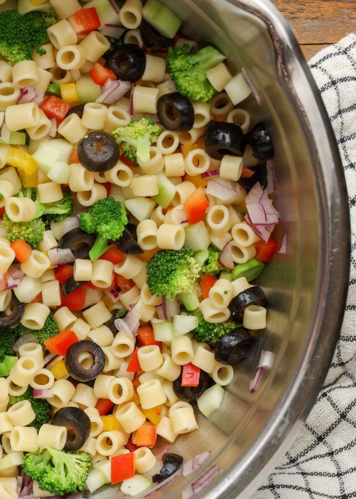 cooked pasta with vegetables in metal mixing bowl with plaid towel