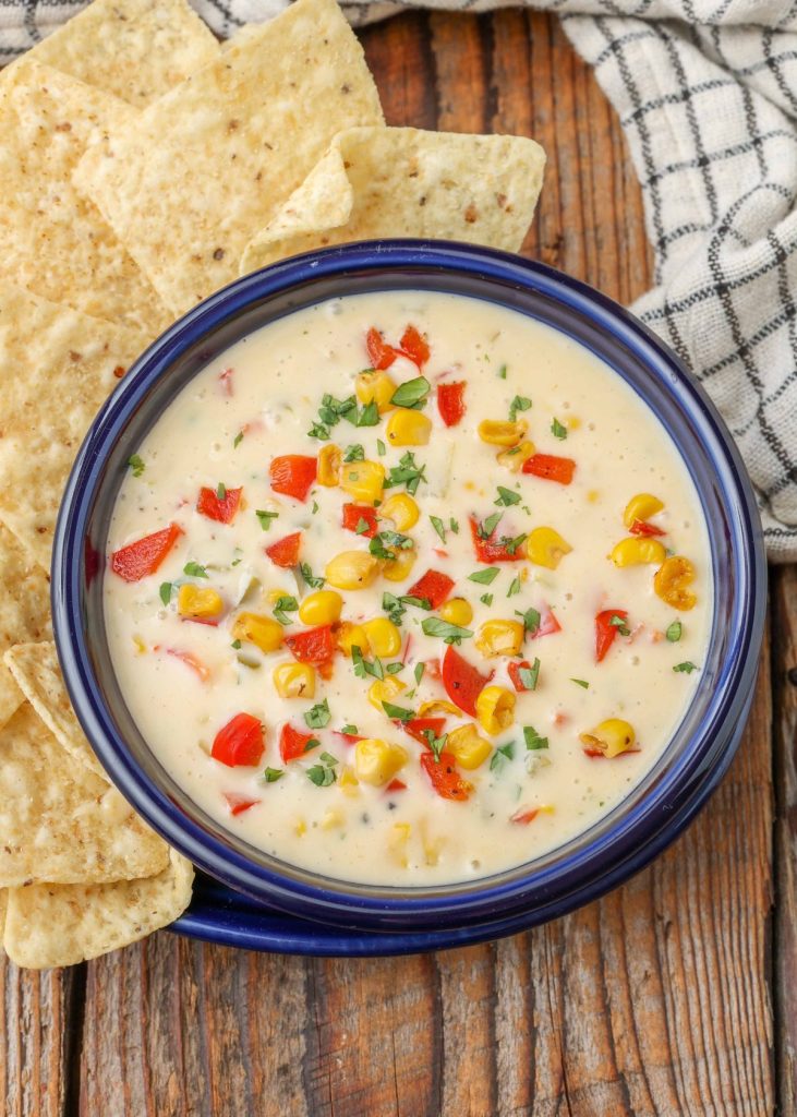 Corn Queso with bell peppers and tortilla chips in blue bowl