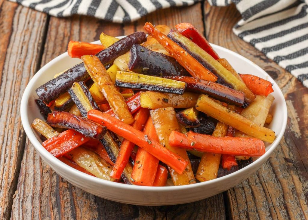 cooked rainbow carrots in white bowl with black and white napkin