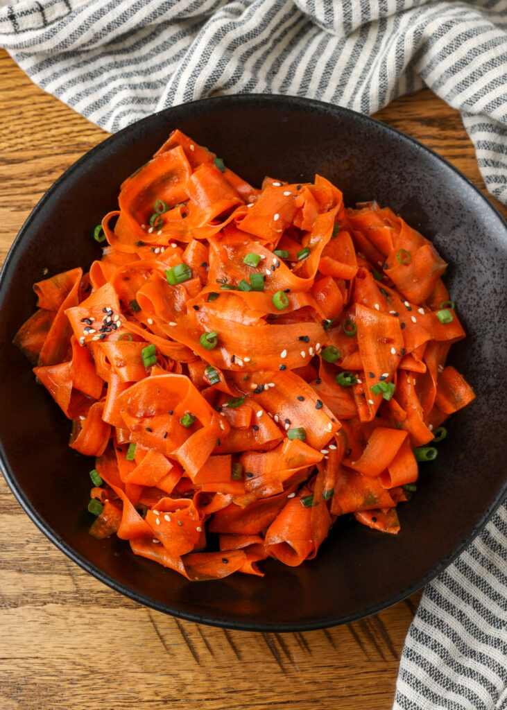 A vertically aligned top down photo of a salad full of thin ribbons of carrots and fresh herbs.