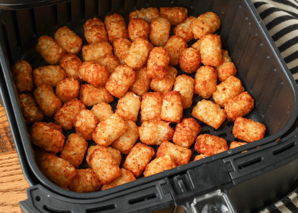 Air fryer tater tots golden brown and crispy in the basket after the second cook, before the cheese goes on.
