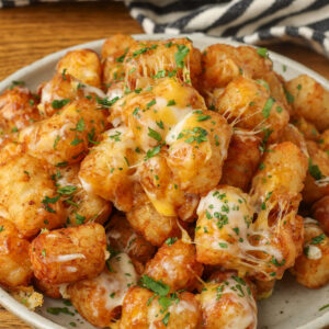 A close up shot of the herbs and cheese on the crispy edges of the tots, piled high on a plate.