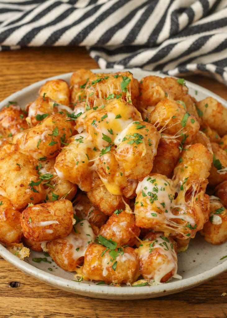 A close up shot of the herbs and cheese on the crispy edges of the tots, piled high on a plate.