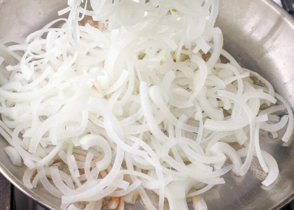 Adding the white slivers of yellow onion to the hot pan.