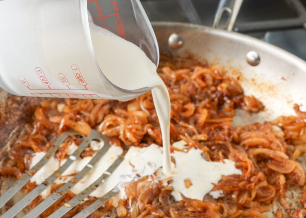An action shot, showing the heavy cream being poured into the pan with the caramelized onions.