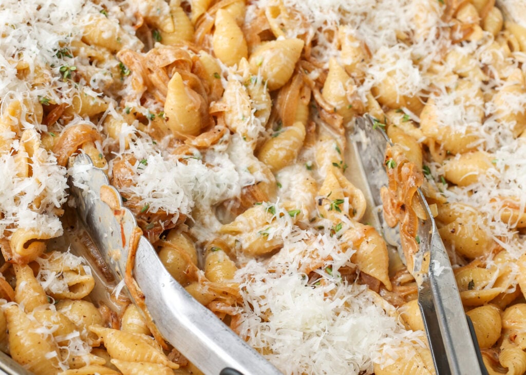Tongs reach down into the pasta, mixing the freshly grated parmesan into the pasta.