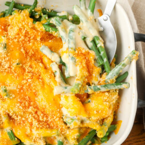 close up photo of cheesy green beans in white baking dish with serving utensil