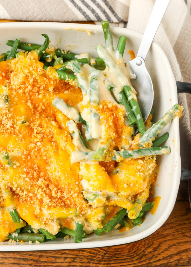close up photo of cheesy green beans in white baking dish with serving utensil