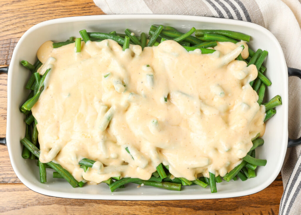 cheese sauce poured over green beans in baking dish