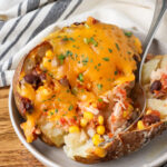 A close up shot of a fork taking a bite out of a loaded chicken baked potato.
