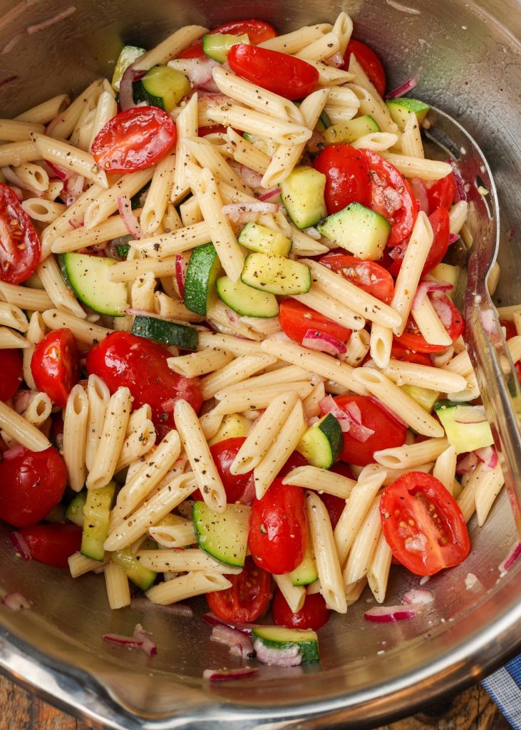 pasta with zucchini and tomatoes in metal mixing bowl