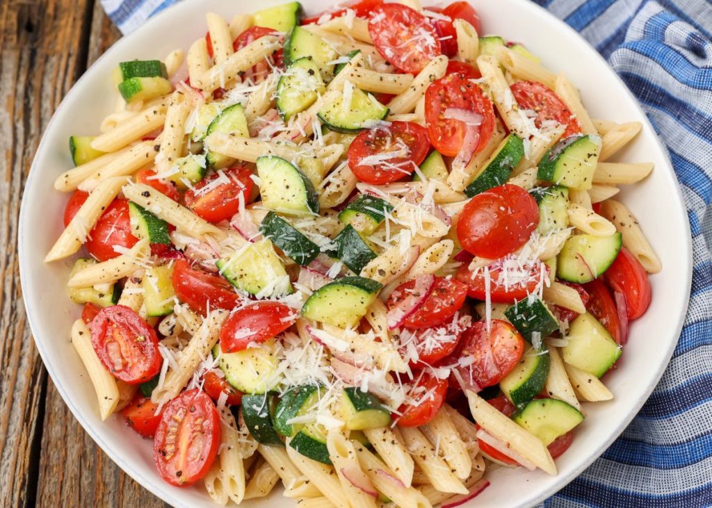 pasta salad with zucchini in white bowl with bowl napkin