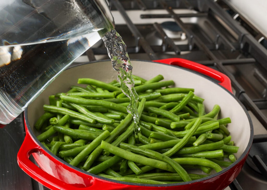 pouring water into pan of green beans on stovetop