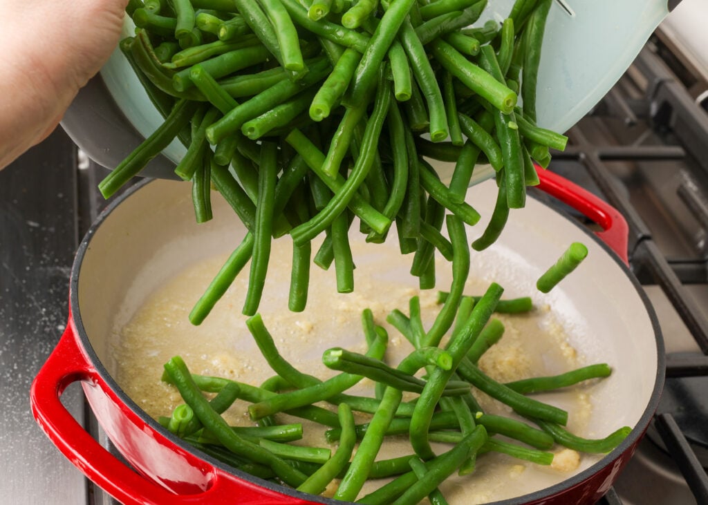 adding green beans to pan on stove