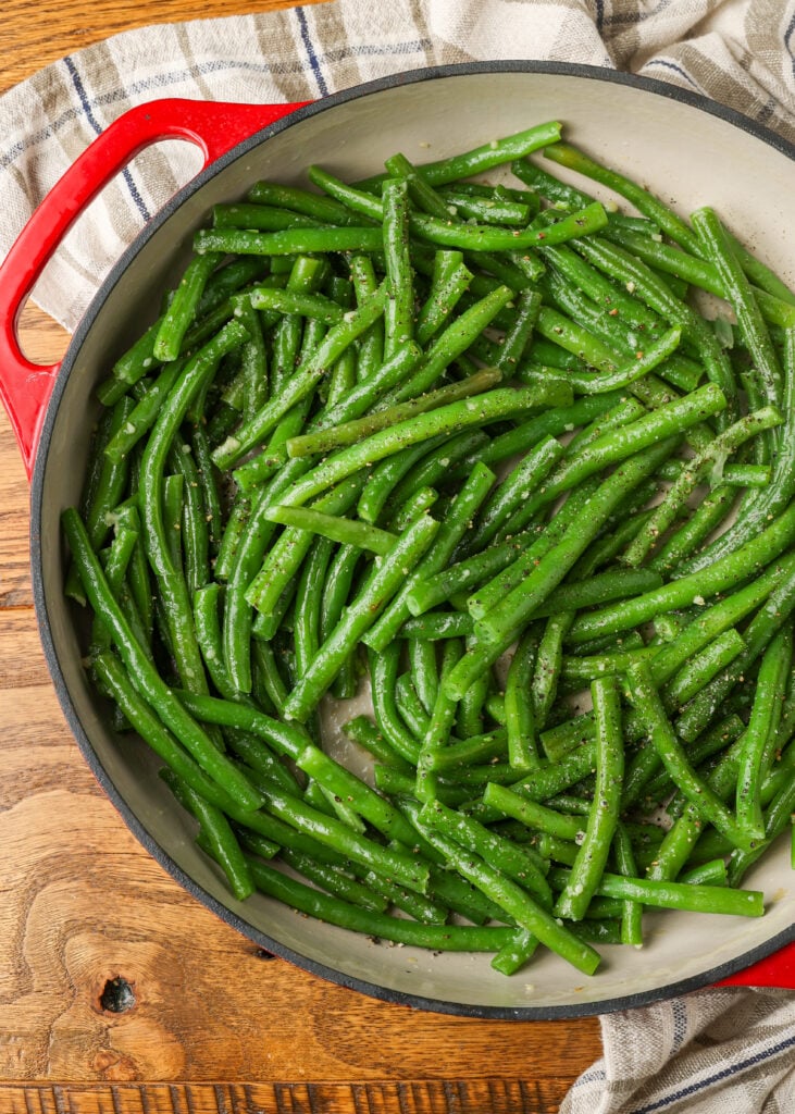 finished green beans in red enamel skillet on wooden table