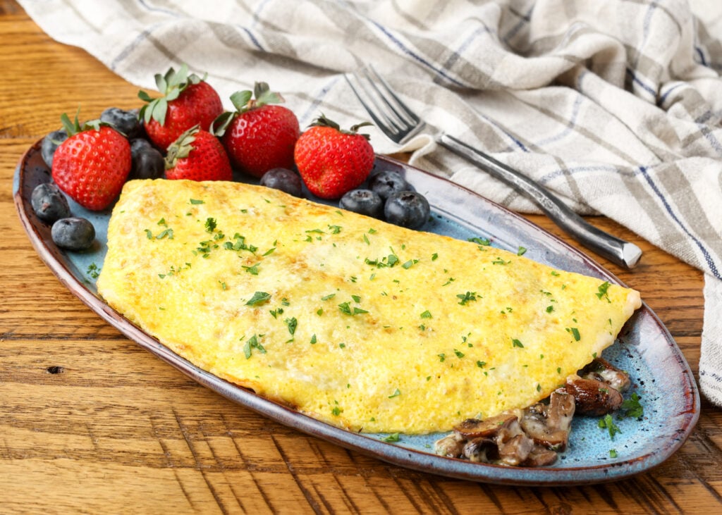 horizontal photo of mushroom omelet on pottery plate on wooden table
