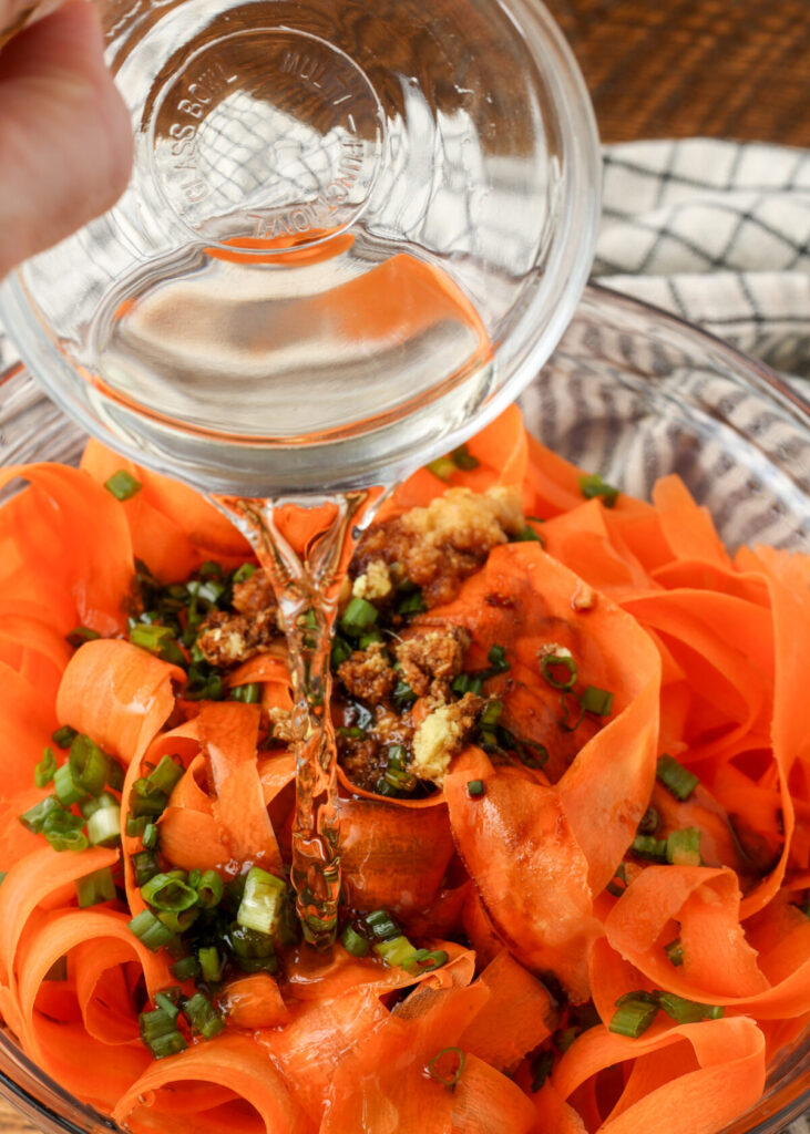 adding vinegar to salad with carrots and onions