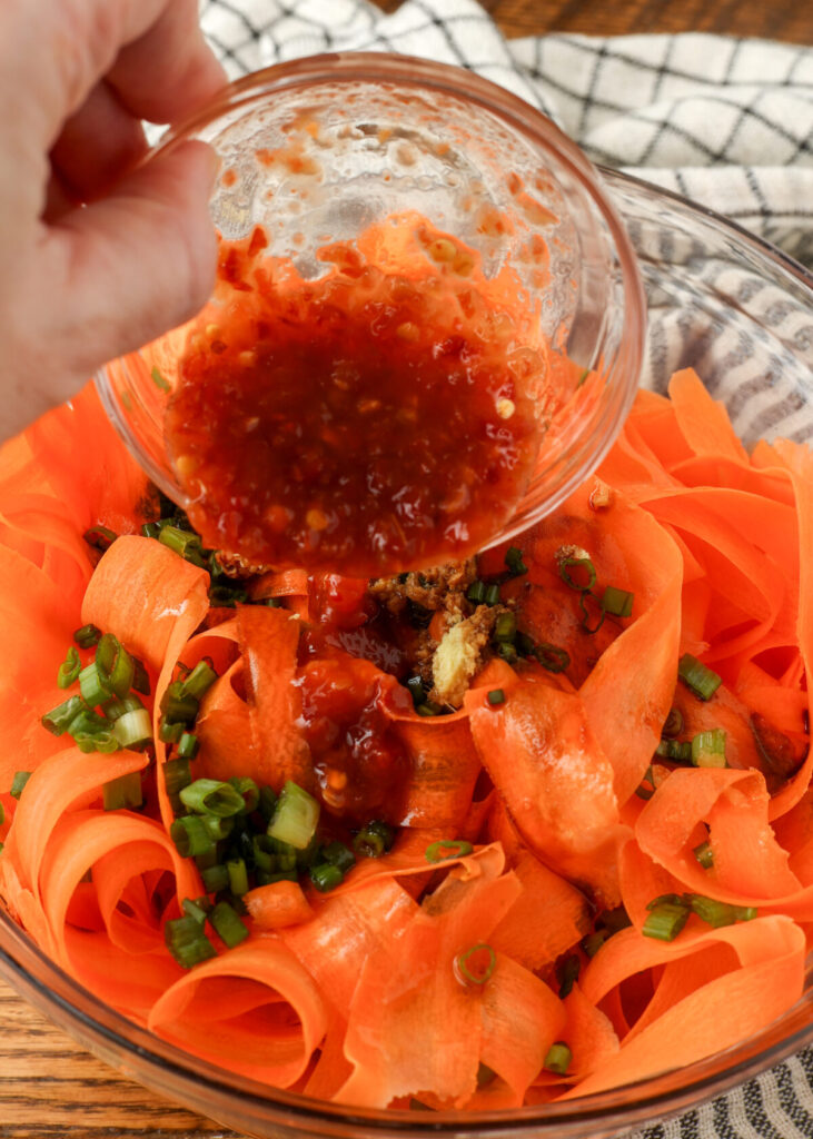adding chili paste to salad with shaved carrots