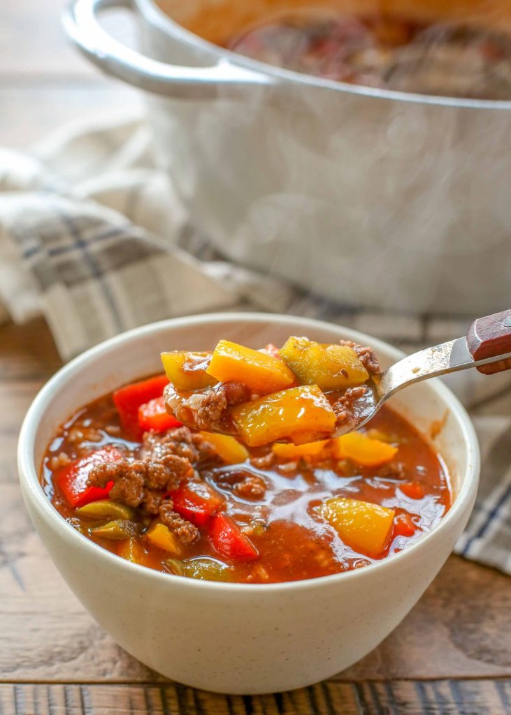 hearty soup with bell peppers, beef, and beans in pottery bowl